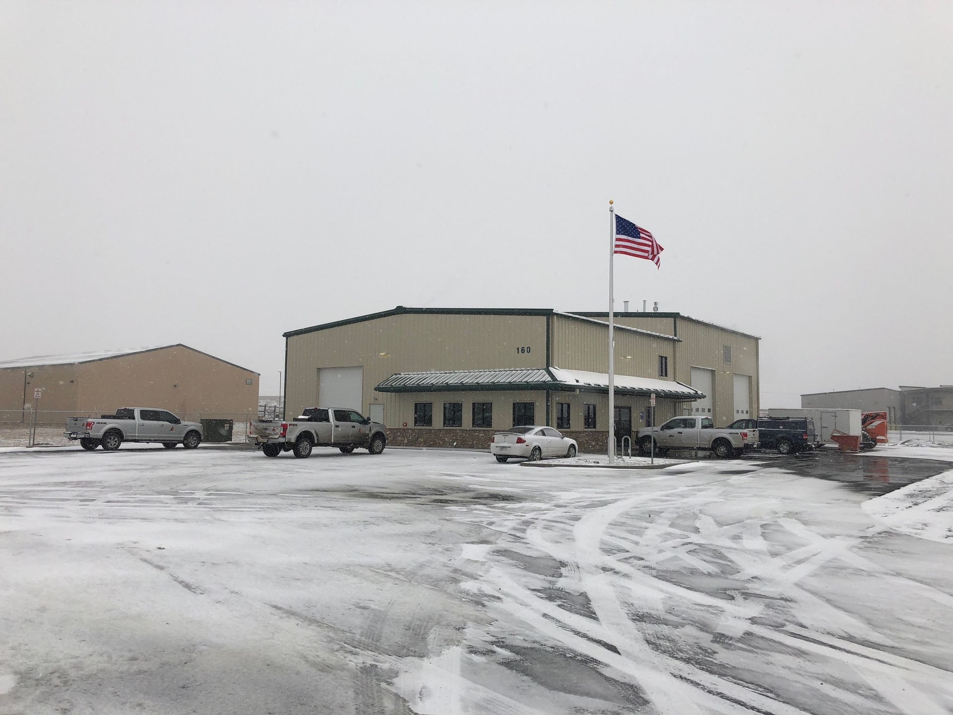 Snowy parking lot outside a beige building with an American flag waving in front.