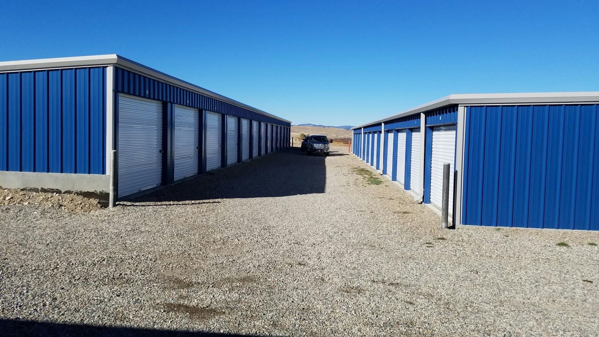 Blue storage units on a gravel lot under a clear sky.