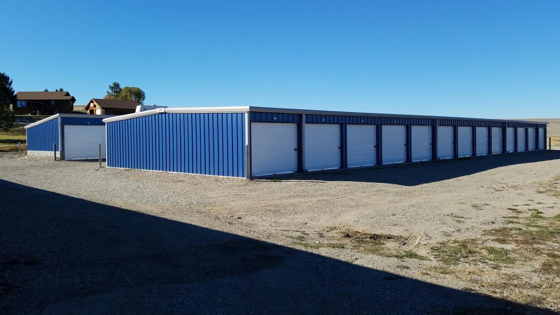 Row of blue-and-white storage units on a gravel lot under a clear blue sky