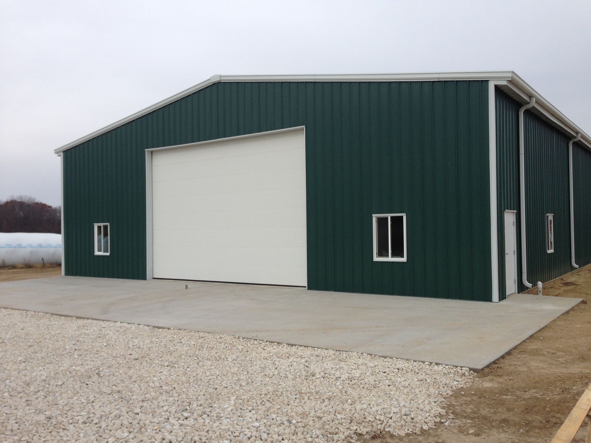 Green metal barn with a large white garage door and gravel driveway.