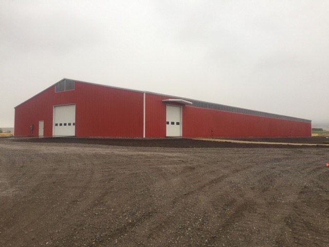 Red metal warehouse with white doors on a gravel lot under a cloudy sky