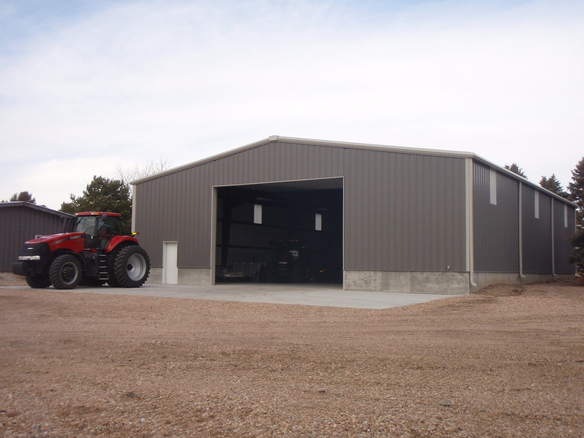 Gray metal barn with an open bay, a red tractor parked beside it, on a gravel lot