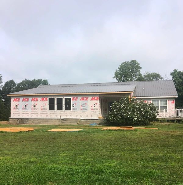 Small single-story building with white siding and a gray metal roof, set in a grassy field under a cloudy sky