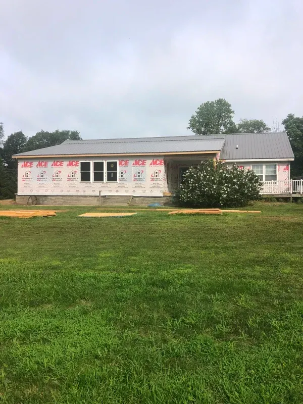 Single-story building with white tarp-covered windows and red lettering, set behind a green lawn under an overcast sky