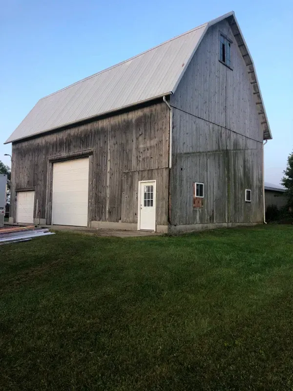 Gray barn with a metal roof and white garage doors on a grassy lot