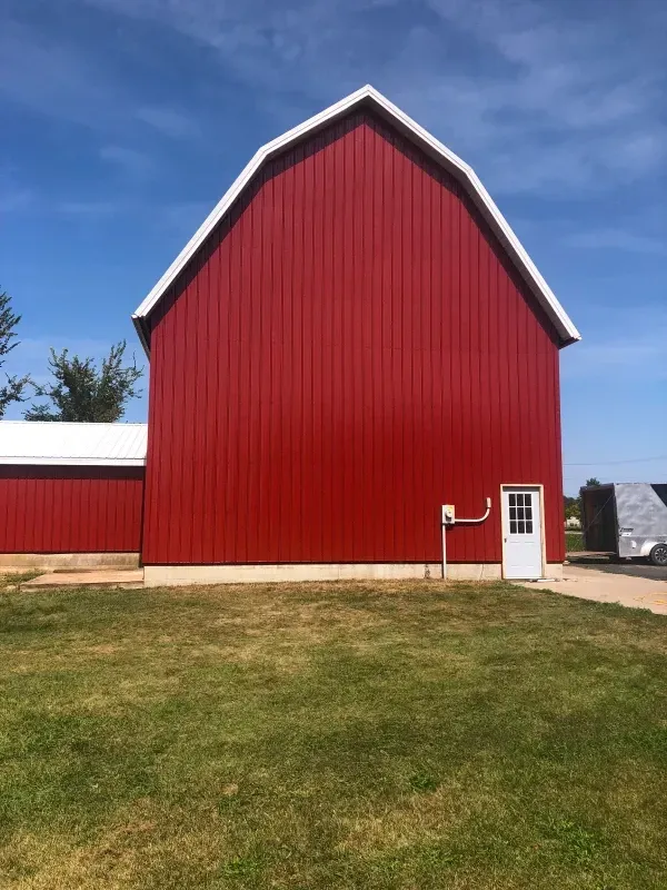 Red barn with white trim and a small white door on a grassy field under a blue sky.