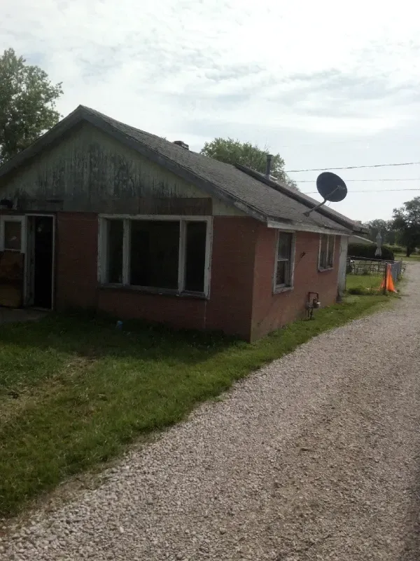 Small brick house with a gravel driveway, satellite dish, and orange cone beside a grassy yard