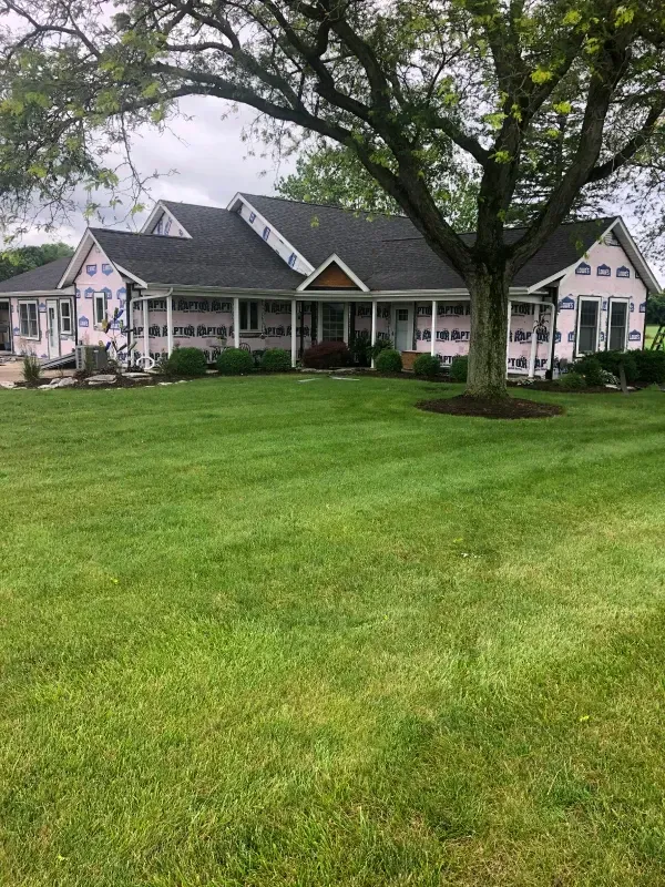 Large white house with a dark roof behind a wide green lawn and two large trees