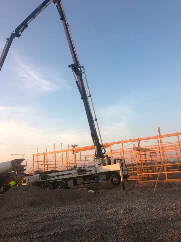Concrete pump truck with extended boom pouring on a construction site at sunset