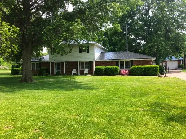 Suburban house with a large green lawn, trees, and a driveway on a sunny day