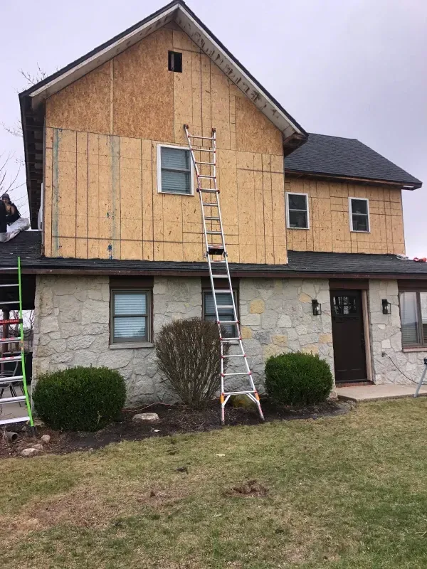 Two-story house with exposed plywood siding and a ladder leaning against the front wall.