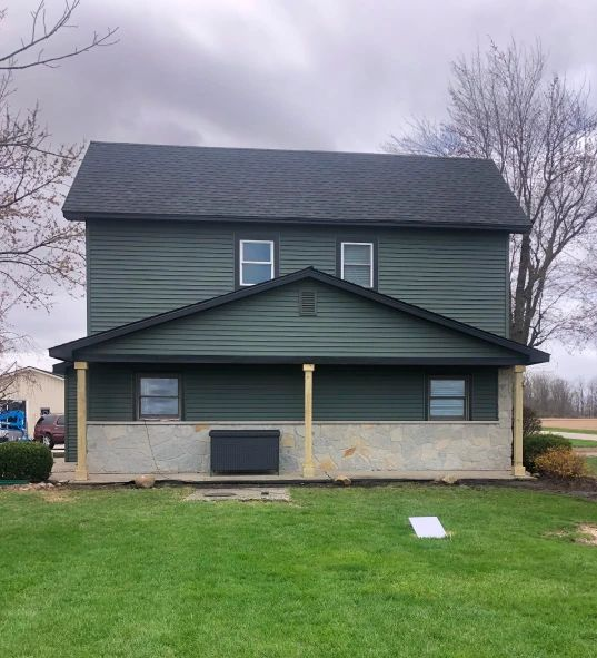 Two-story house with green siding, a gray roof, and a covered front porch above a grassy yard.