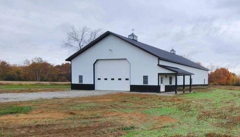 White barn with large garage door in a rural field under a cloudy sky