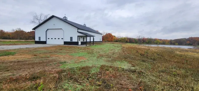 White barn with garage doors on a grassy hillside under overcast sky