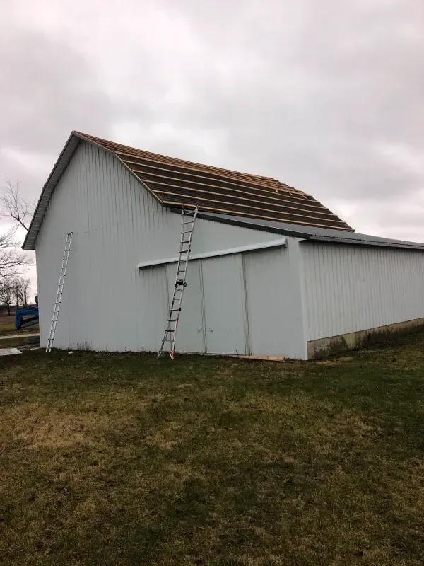 White barn with a ladder leaning against the side under an overcast sky