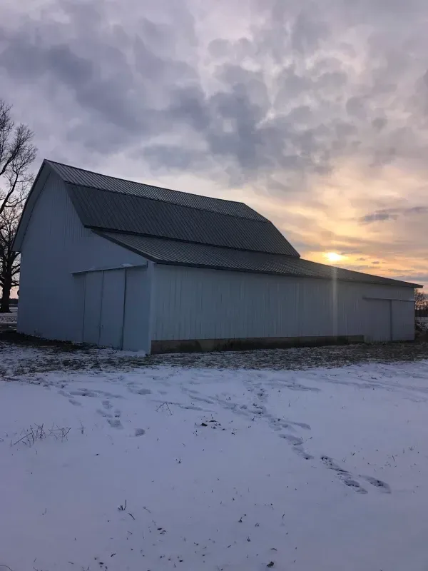 Snow-covered barn at sunset under a cloudy sky
