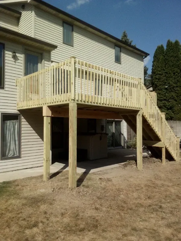 Backyard wooden deck with stairs attached to a two-story house, over a dry yard