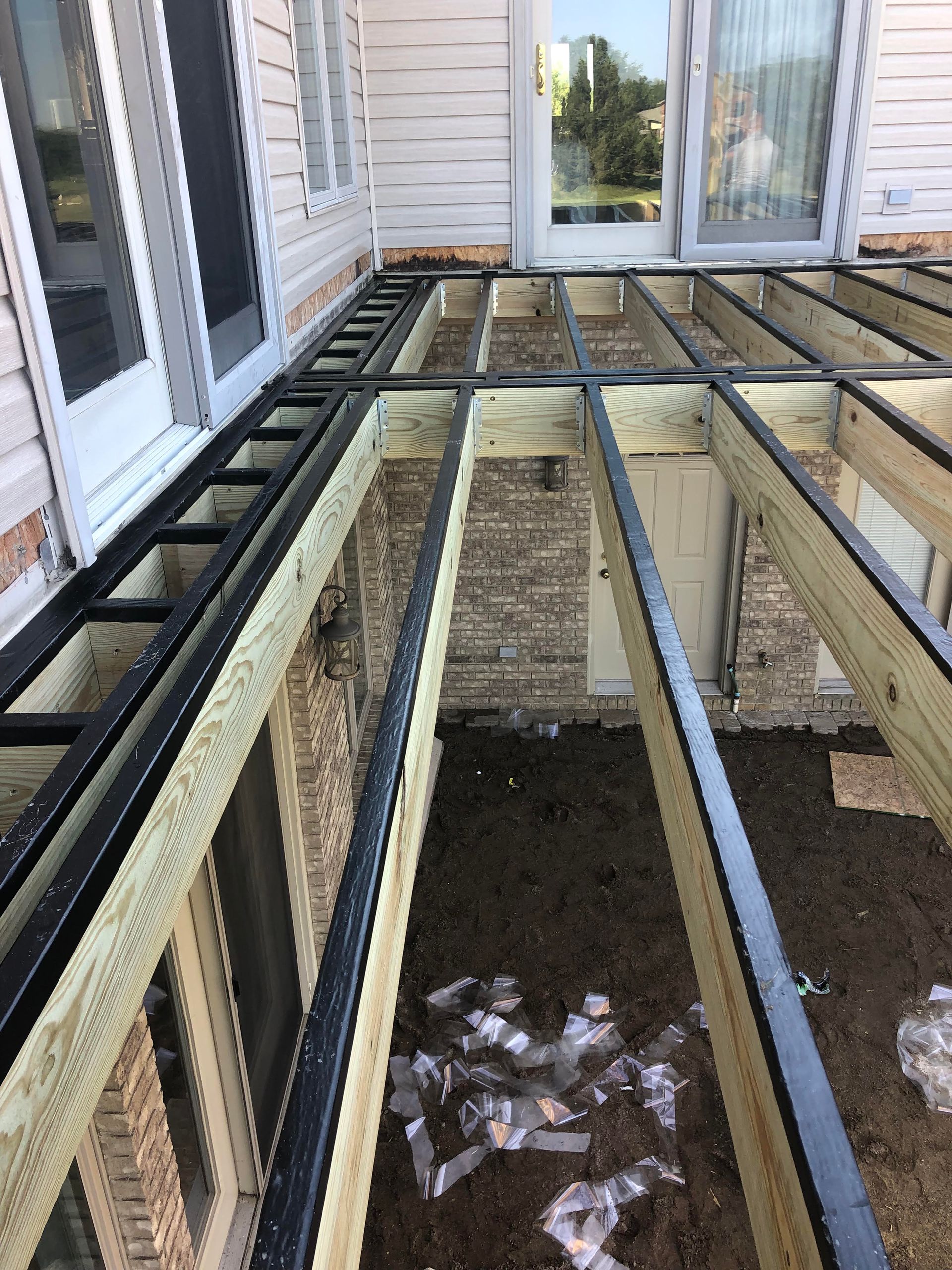Partially demolished deck with exposed joists beside a brick house and white siding