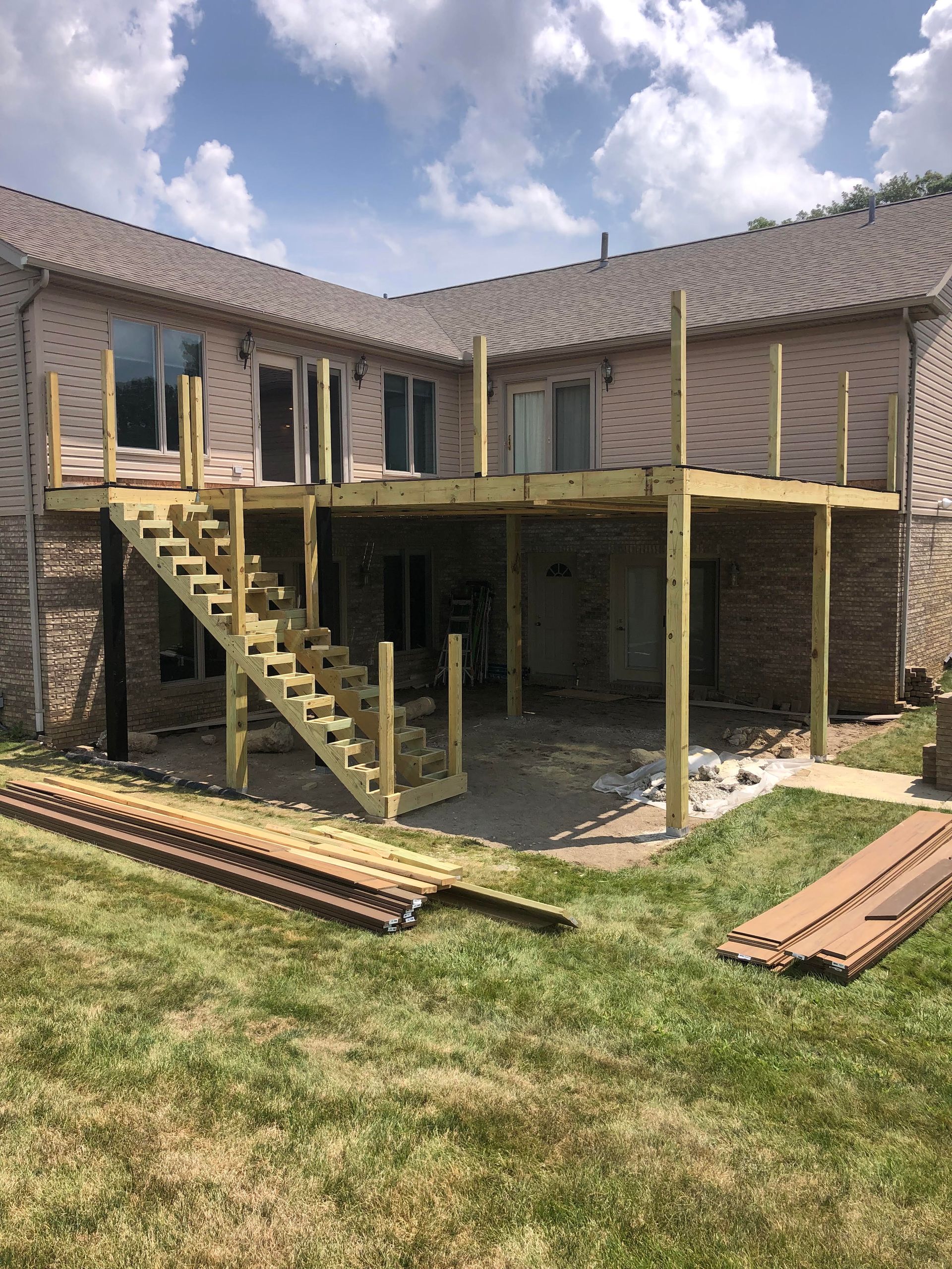 Partially built wooden deck and stairs attached to a brick house under a cloudy sky