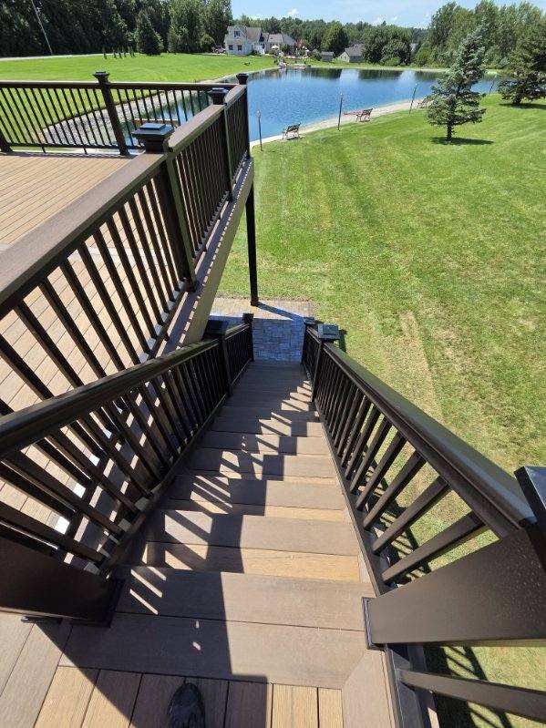 Wooden stairs descend to a grassy lakeside dock with black railings and blue water beyond.