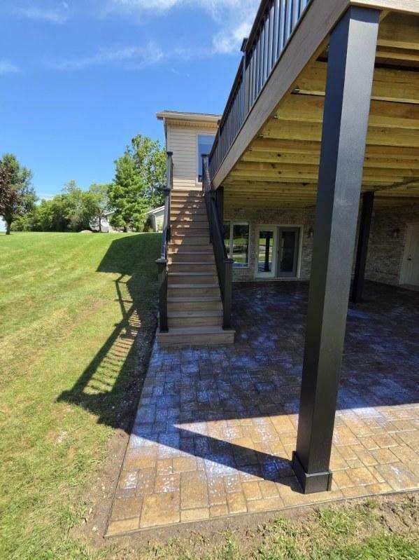 Back patio with brick pavers, stairs to an upper deck, and a grassy lawn beside a stone wall.