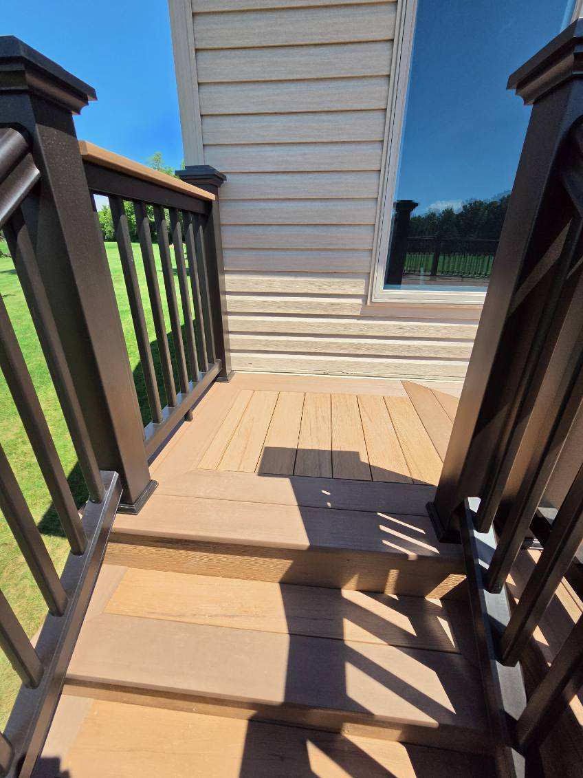 Wooden deck stairs with dark railings leading to a small landing beside a beige house wall.