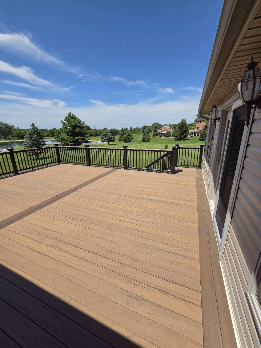 Spacious wooden deck overlooking a green field under a blue sky, beside a house with a lantern.