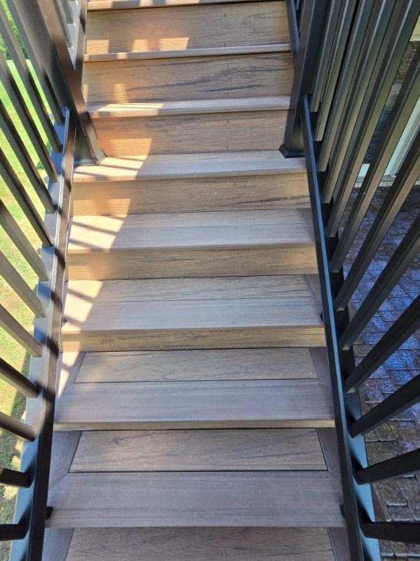 Wooden outdoor staircase with black metal railings in sunlight