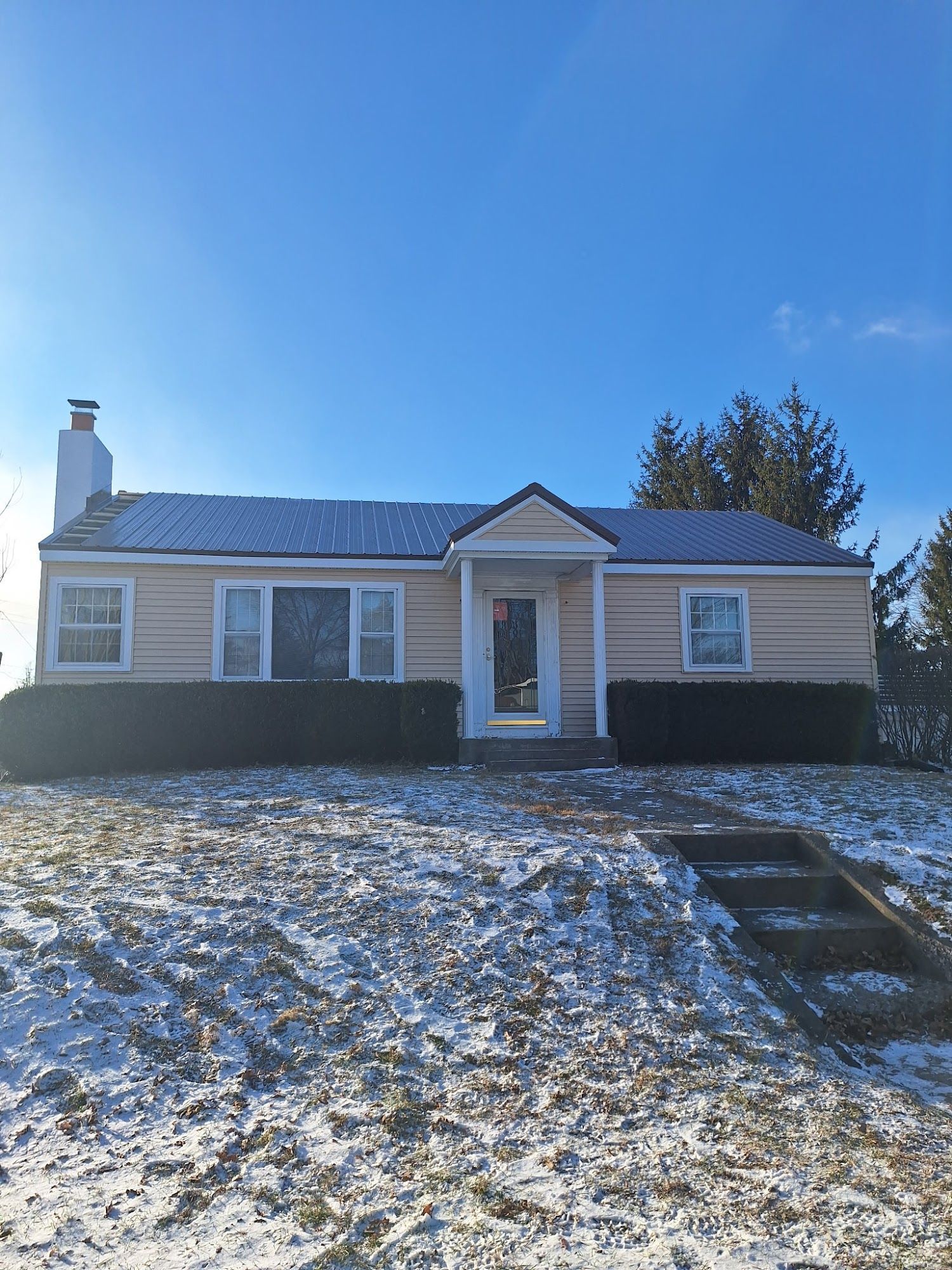 A small, yellow house with a metal roof on a snow-covered hill under a clear, blue sky.