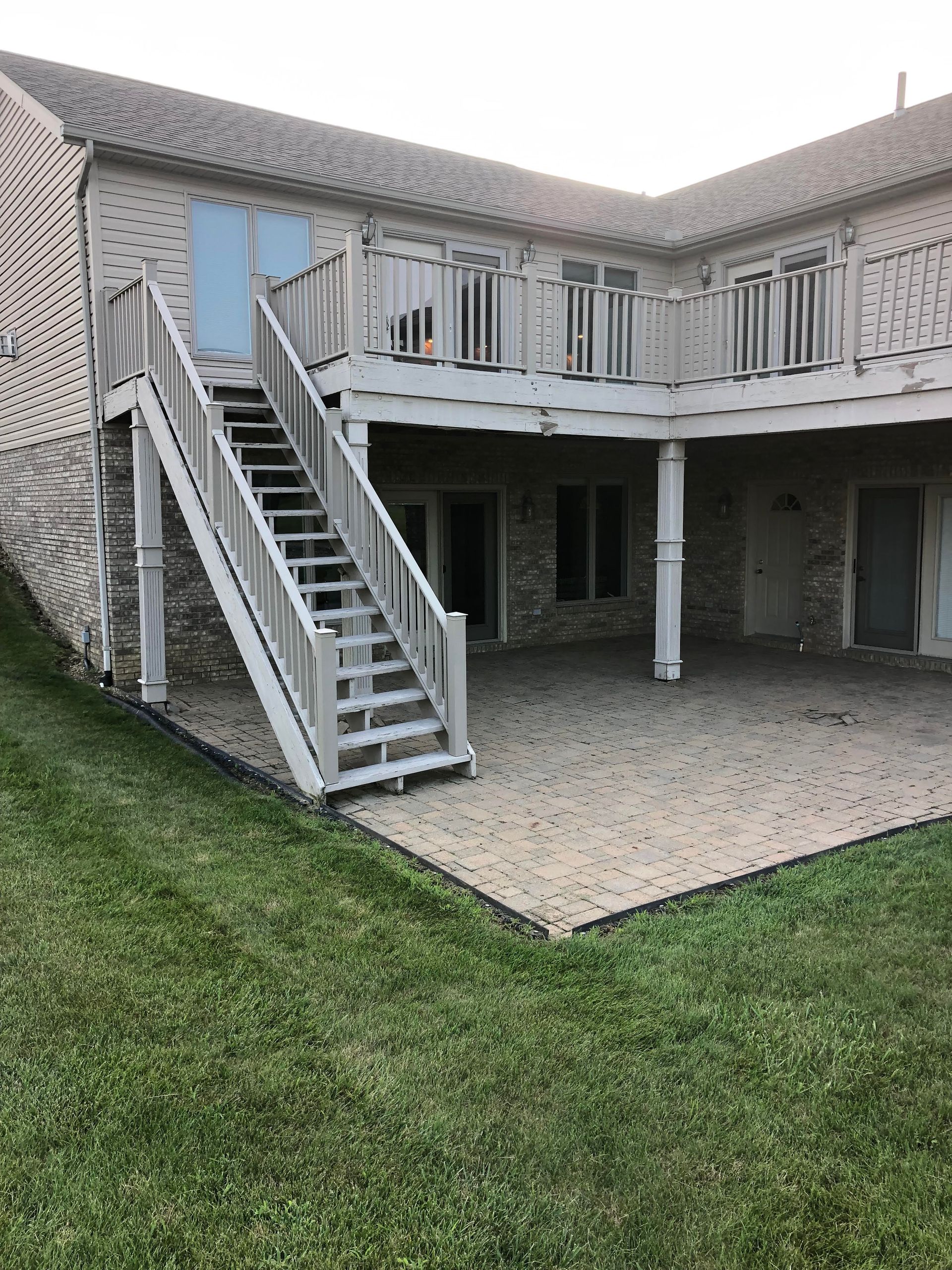 Exterior of a two-story house with an upper balcony, stairs, and a covered patio below