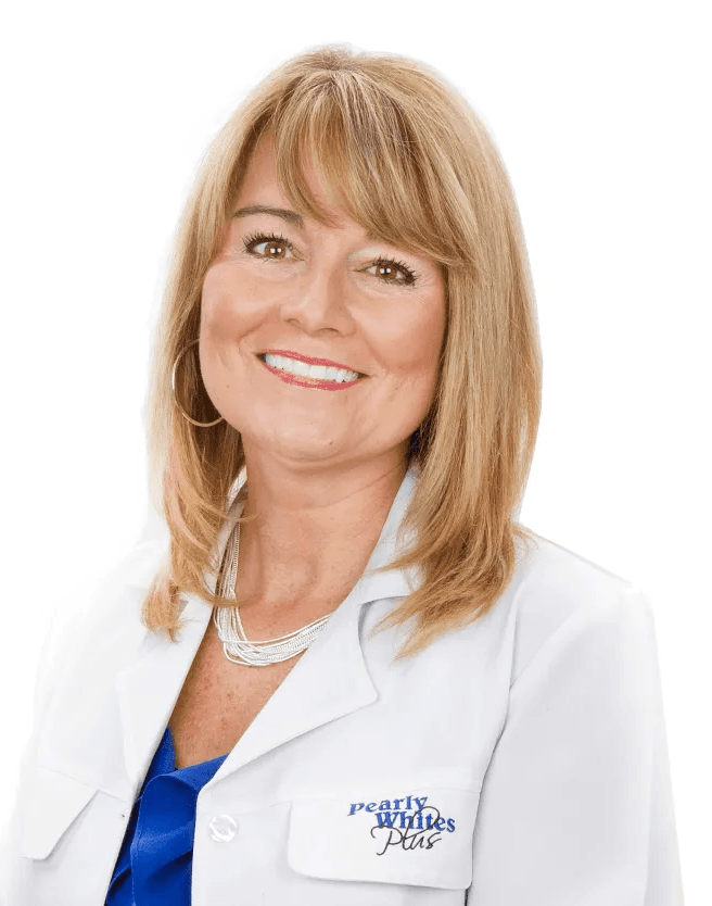 A woman wearing a white lab coat and a blue shirt is smiling.