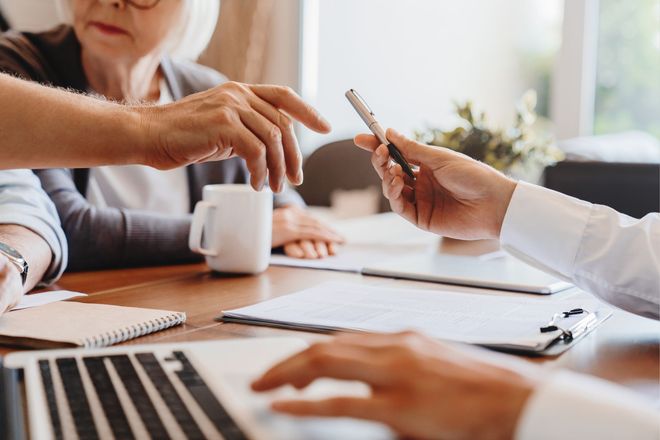 Person handing a pen to someone at a table with documents and a laptop. Person handing a pen to someone at a table with documents and a laptop.