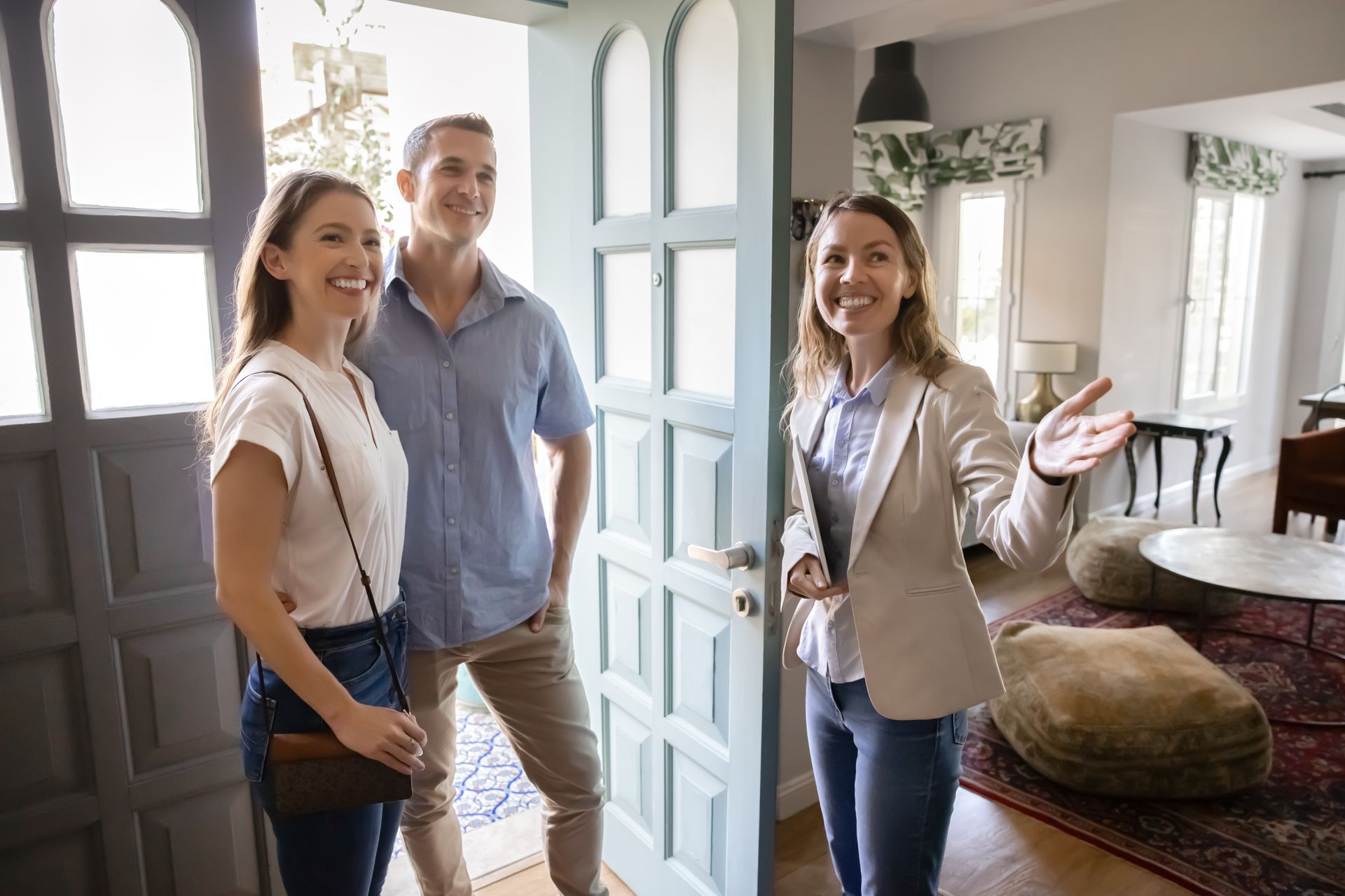 Real estate agent welcomes a couple into a home. They are smiling.