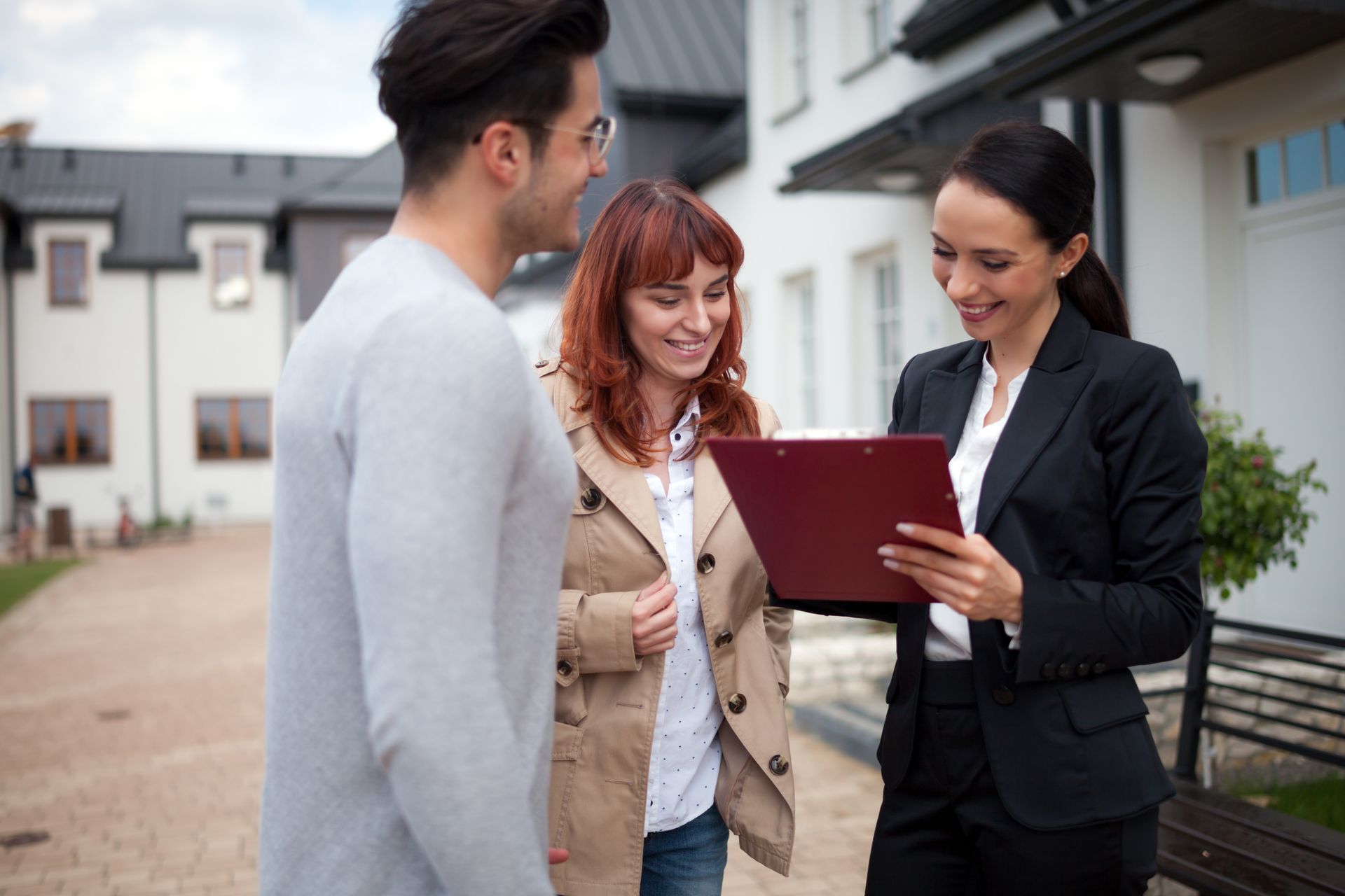 Real estate agent showing paperwork to a couple outside a house.