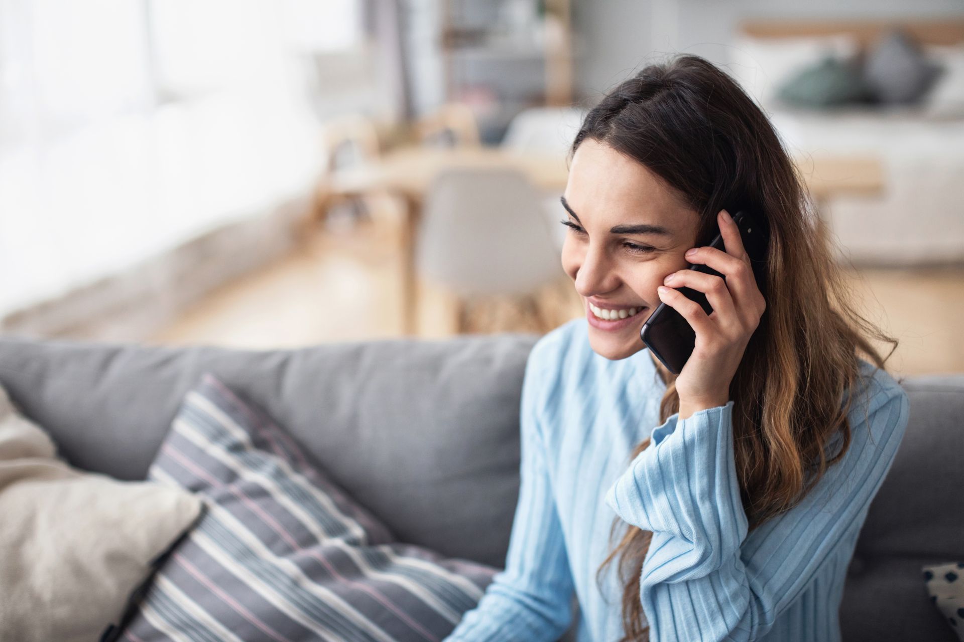 Woman sitting on a couch, smiling while talking on a cell phone. Living room background.