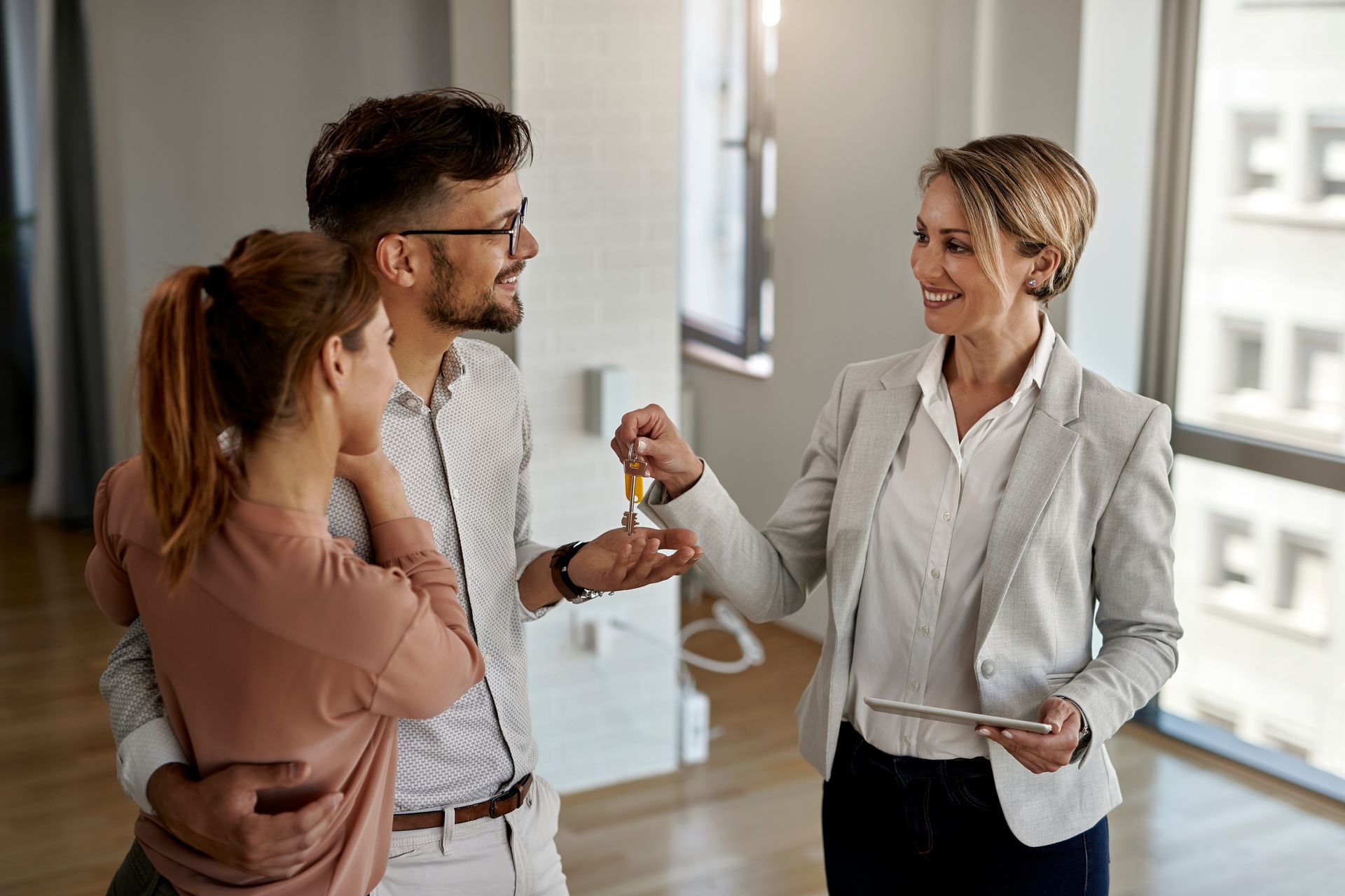 Real estate agent handing keys to a couple in a new home; hugging, smiling.