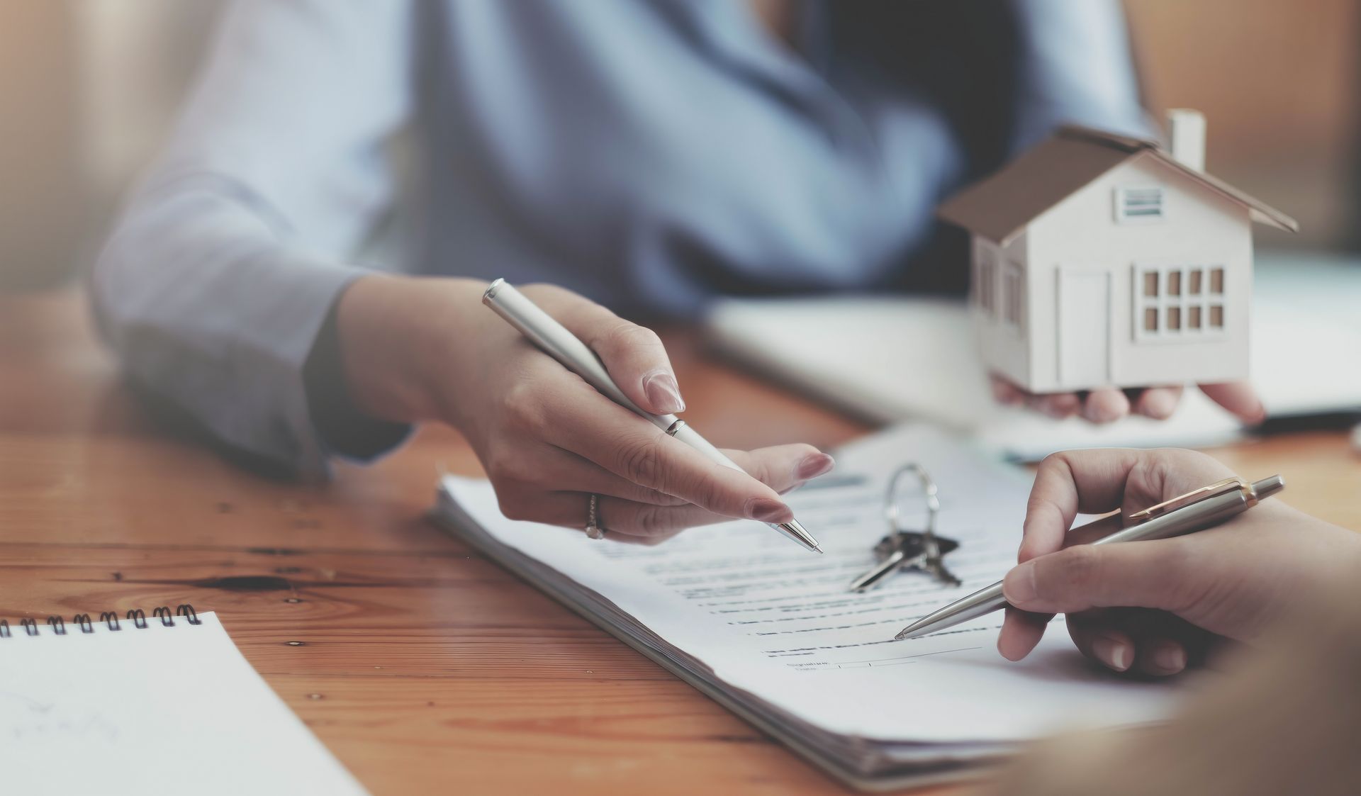 Hands signing a document, miniature house held nearby, keys on the table. Hands signing a document, miniature house held nearby, keys on the table.