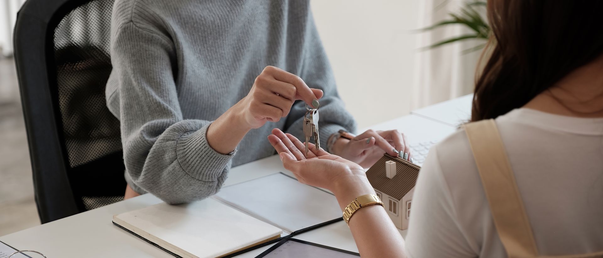 Person handing house keys to another person at a desk.
