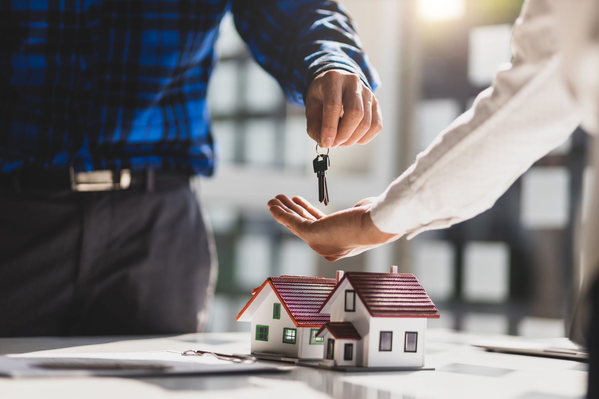 Person handing house keys to another over a model home. Person handing house keys to another over a model home.