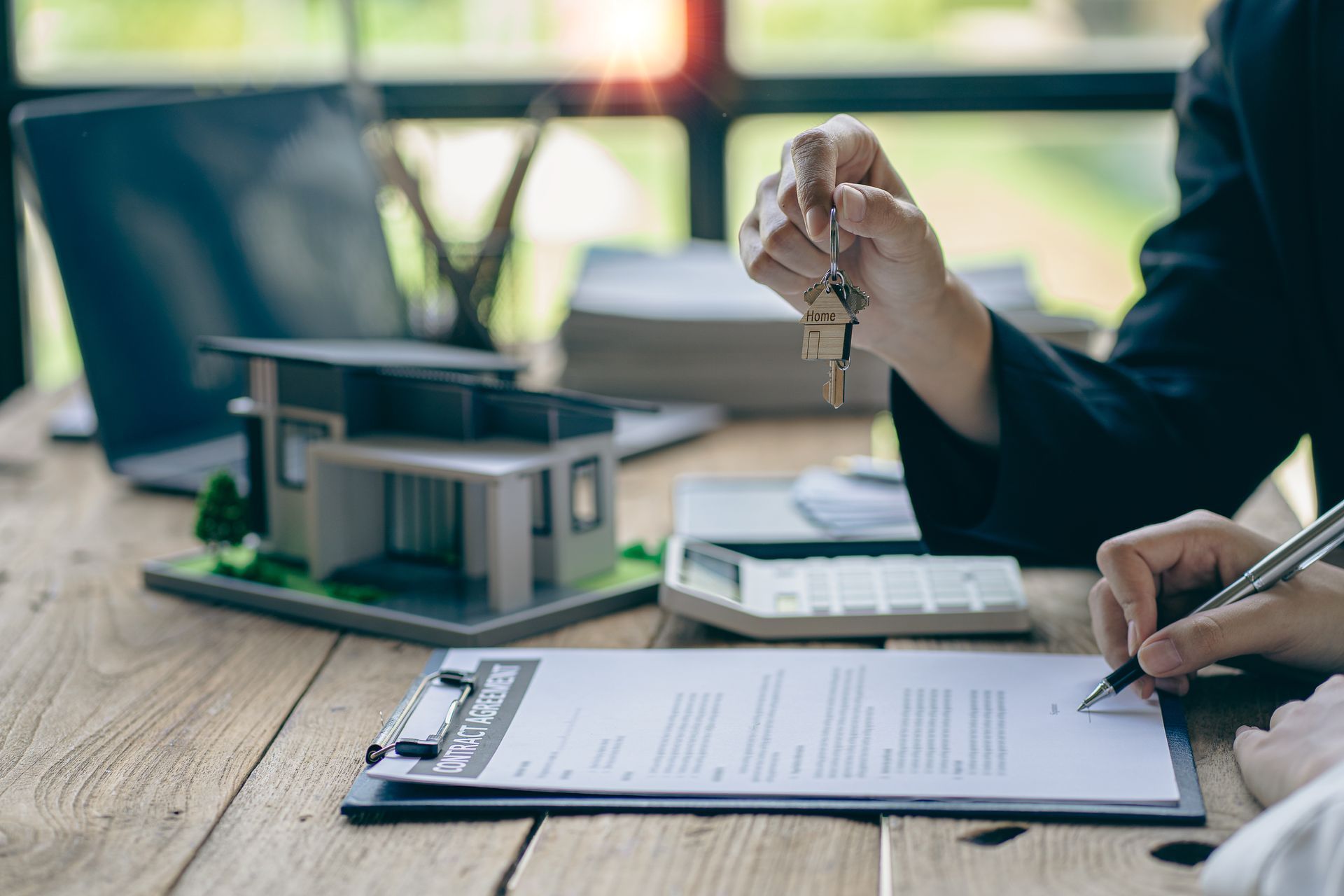 Person handing keys over a signed real estate document next to a house model.