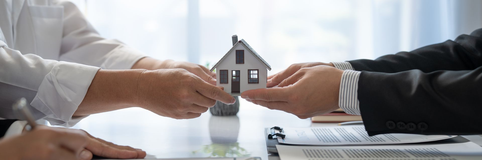 Hands passing a small house model over a table. A business deal or transaction. Hands passing a small house model over a table. A business deal or transaction.
