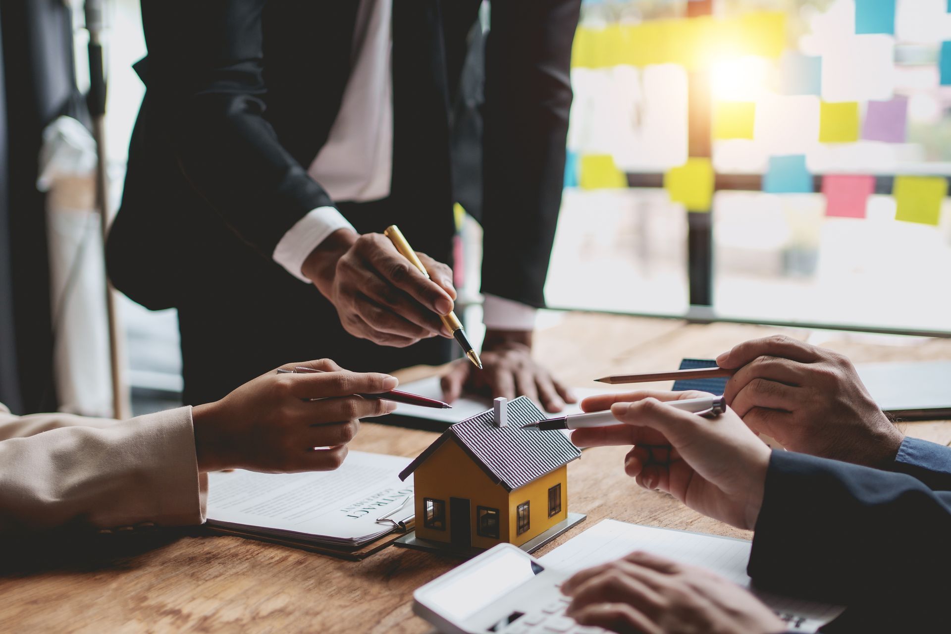 Businesspeople discussing a miniature house, pointing at documents, suggesting a real estate deal.