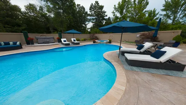 Outdoor swimming pool with lounge chairs, umbrellas, and hot tub.
