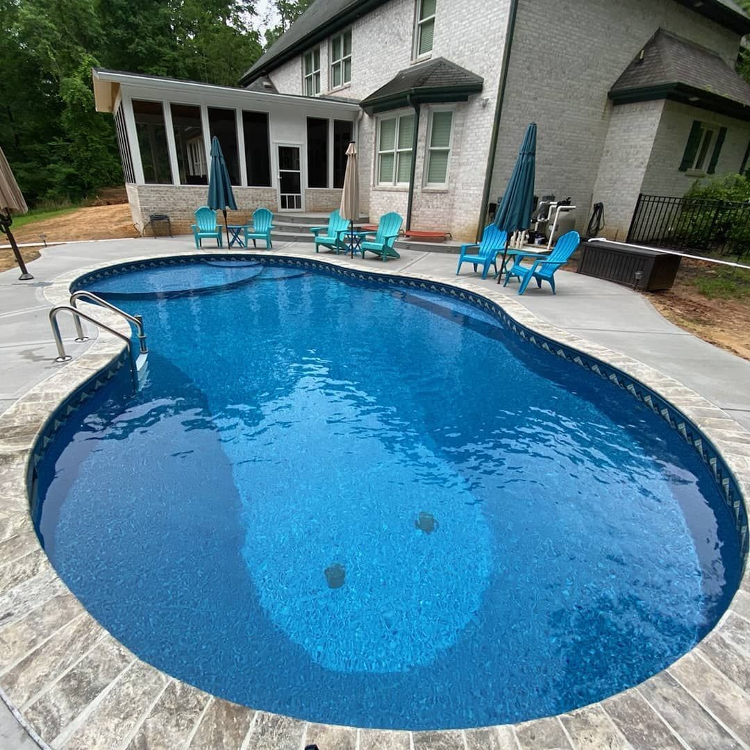A kidney-shaped swimming pool with blue water and surrounding patio, near a two-story house with blue chairs.