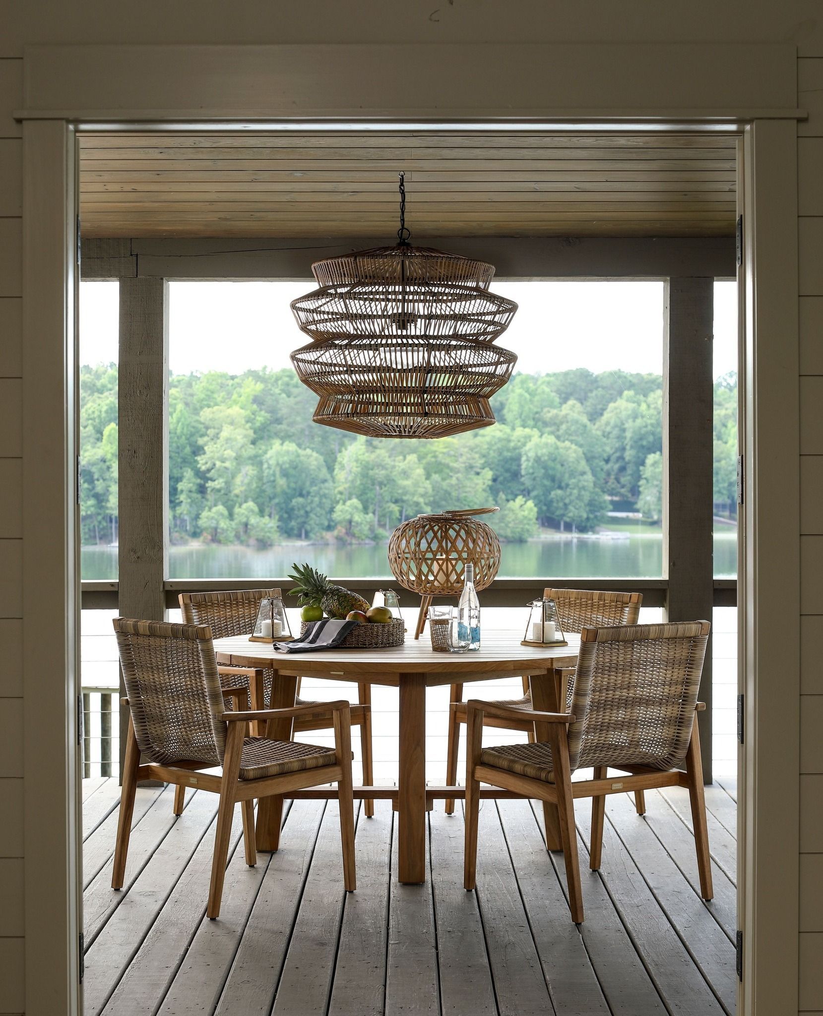 Outdoor dining set: round weathered wood table, chairs with cushions, potted palm, pineapple.