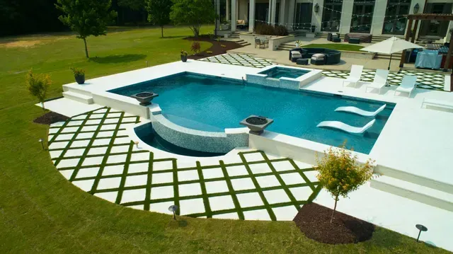 Aerial view of a luxury pool area with a blue pool, spa, white deck, and checkered lawn.