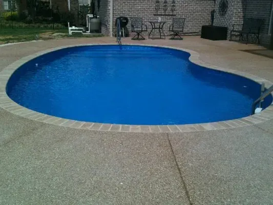 Pool with blue water, surrounded by a concrete deck and brick edging; outdoor setting.
