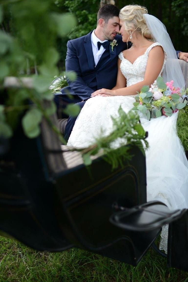 Bride and groom sitting together outdoors on a black bench, leaning close in wedding attire.