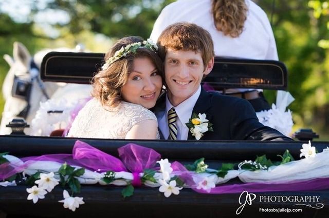 Newlyweds smiling in a decorated golf cart, with white flowers and a purple ribbon