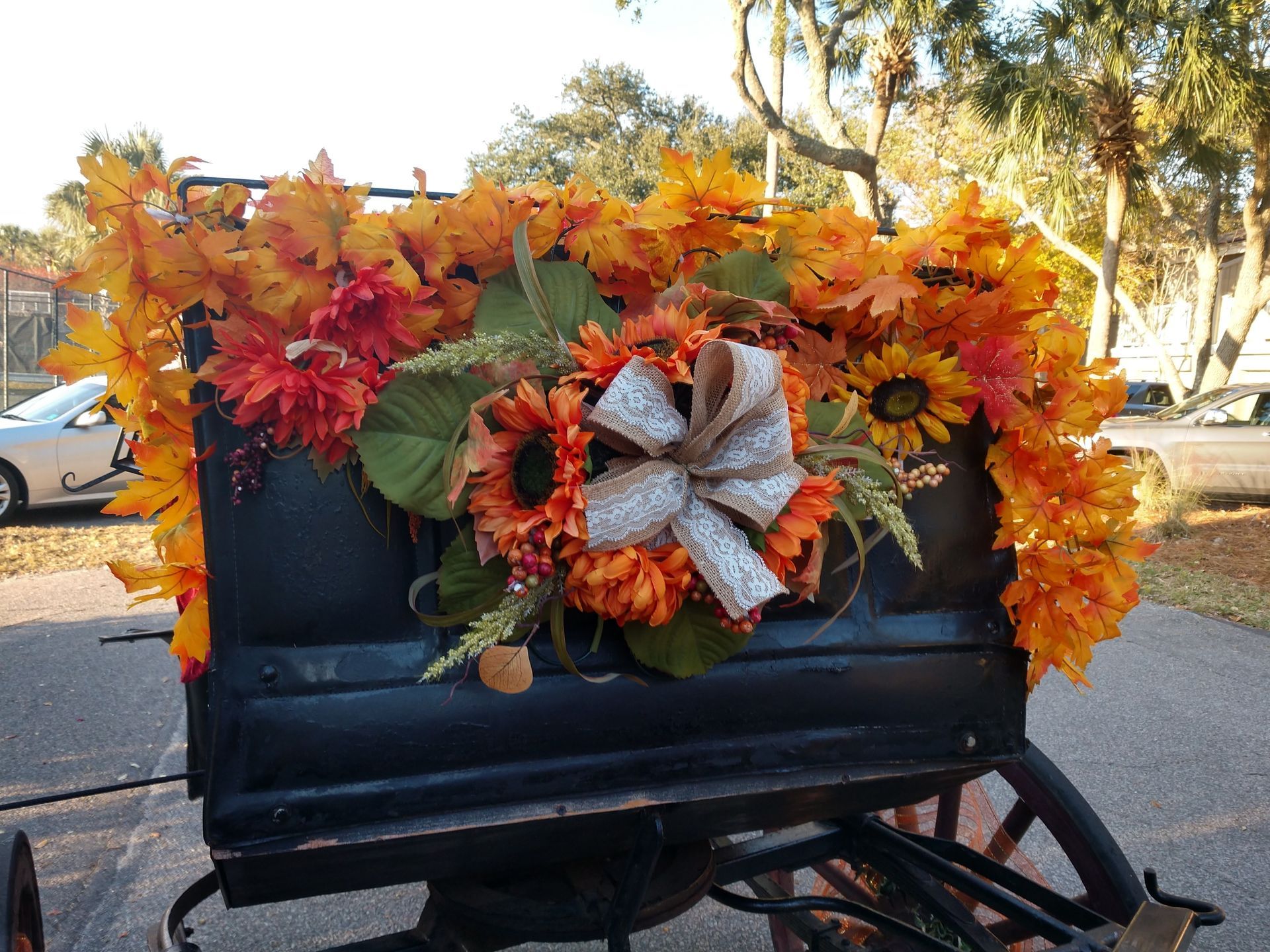 Black wagon decorated with autumn leaves, sunflowers, and a burlap bow outdoors
